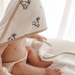 Bébé enveloppé dans une cape de bain blanche à motifs koala, allongé sur un linge blanc.