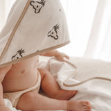 Bébé enveloppé dans une cape de bain blanche à motifs koala, allongé sur un linge blanc.